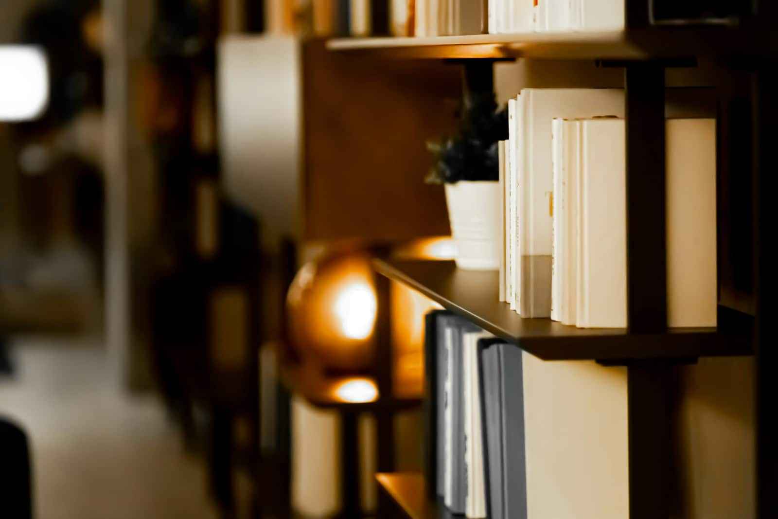 Wooden bookshelves in a dim room, with a lamp glowing among the books