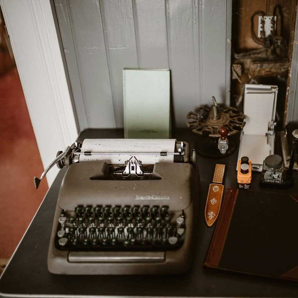 An old typewriter on a dark wooden desk beside papers and a pen