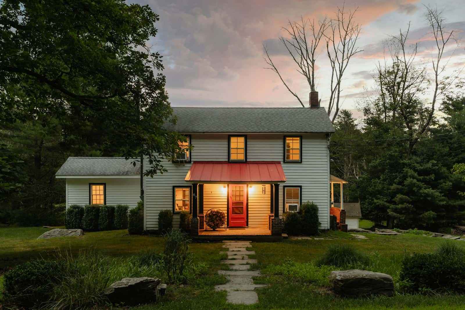 A white clapboard family home in upstate New York at dusk, its windows lit and the porch light on