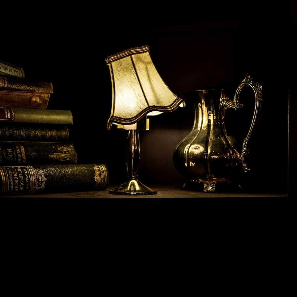 A brass table lamp glowing beside a stack of old leather-bound books in the dark