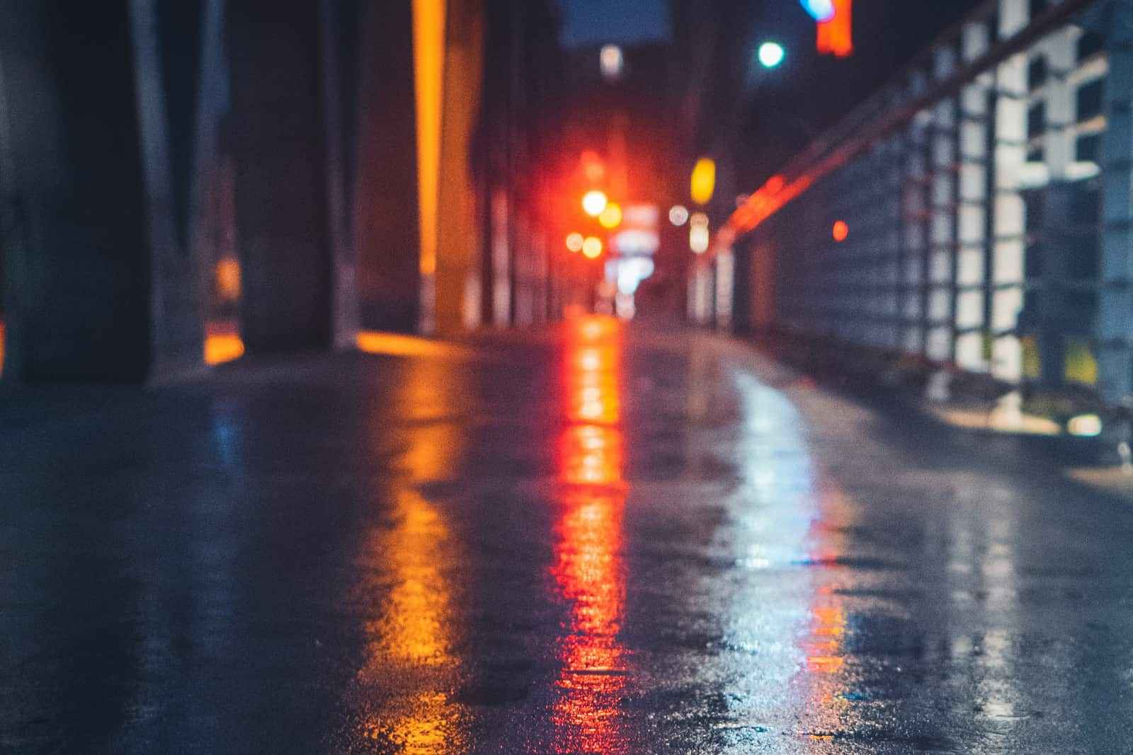 A wet road at night with red and amber lights reflected on the pavement