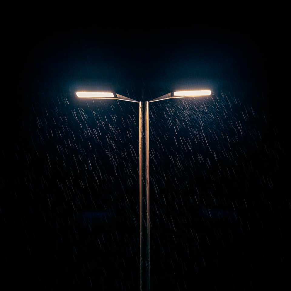 A streetlight glowing above a dark road in steady rain at night