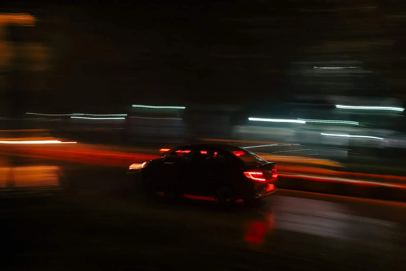 A car on a highway at night, its tail lights streaking