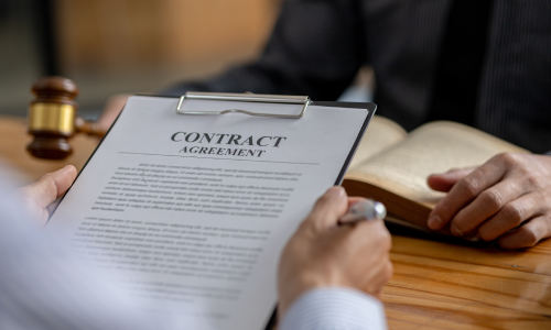 A man is reading a contract agreement, and in front of him is another man who is reading a book.