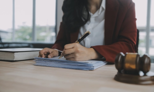 A woman attorney writing notes on paper documents with a blurred gavel in the foreground.