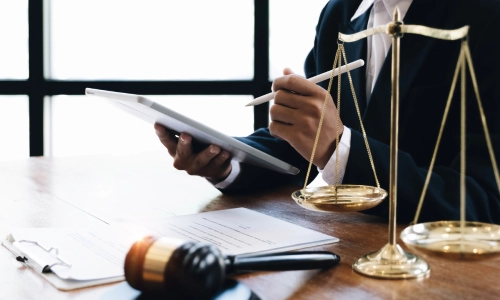 A lawyer holding a tablet in one hand and a stylus on the other while sitting at their office table with a file on top of the desk.