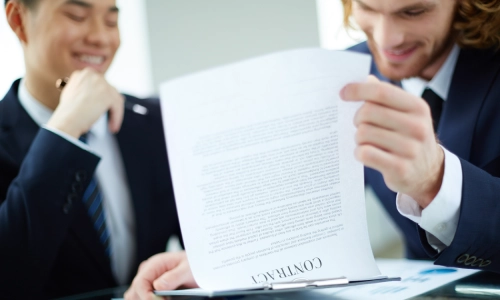 Two men in suits flipping through pages and reviewing contract documents.