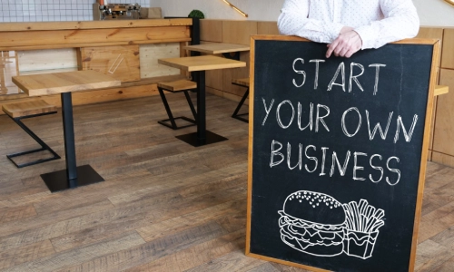 A budding entrepreneur standing with a chalkboard sign promoting the journey of starting a business.