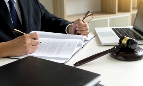 Albany Business Success Planning Lawyer holding a pair of glasses in the left hand and a pen in the right while signing documents
