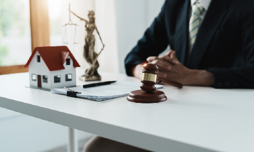 Real Estate lawyer sitting with hands together in front of an office desk with a model house on top of it.