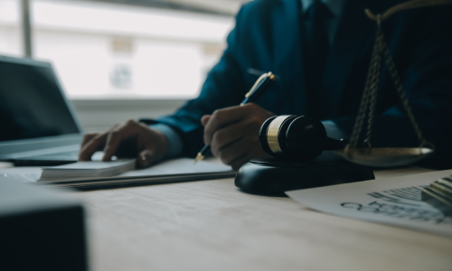  Close-up of a New York employment contract lawyer reviewing case files and signing documents in his office while sitting down.