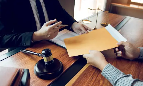 A man handing a document to a New York wills lawyer, with a gavel and scales of justice on the table.