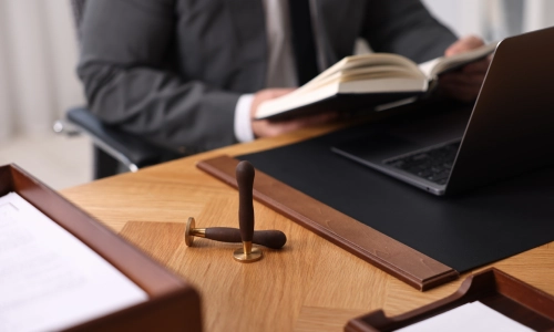 A New York general counsel lawyer at his desk with a laptop, a book, and a document stamp.