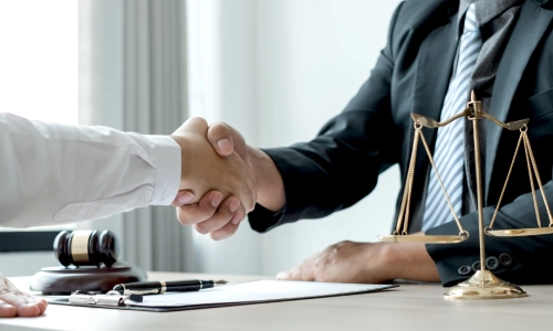 A Glens Falls business lawyer is shaking the hand of a satisfied client as they sit on opposite sides of an office desk