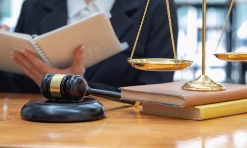 A small business lawyer serving Glens Falls reads a notebook in their right hand with a hammer and gavel and scales sit in the foreground